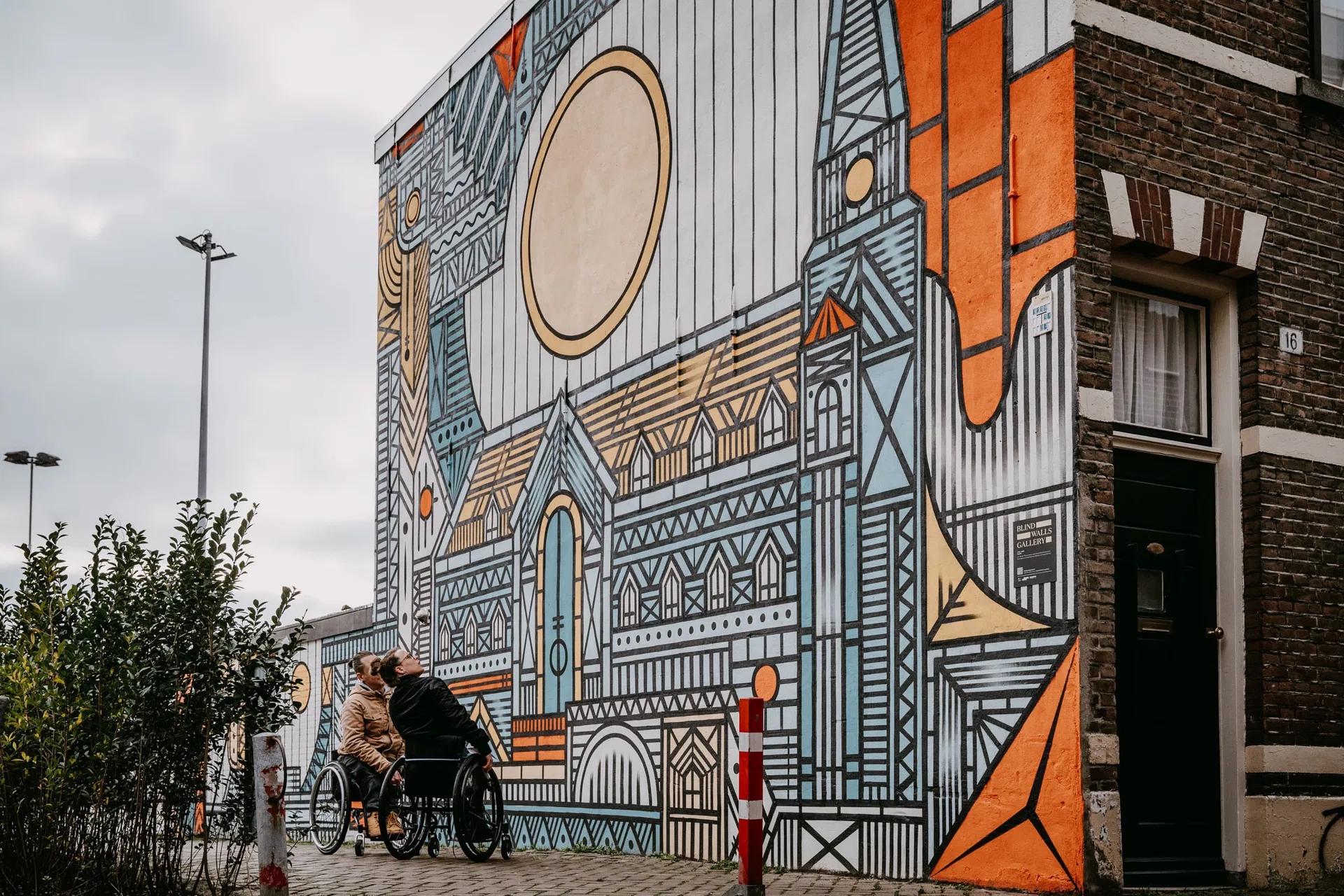 Picture of two persons in a wheelchair admiring a blind wall (mural) in Breda