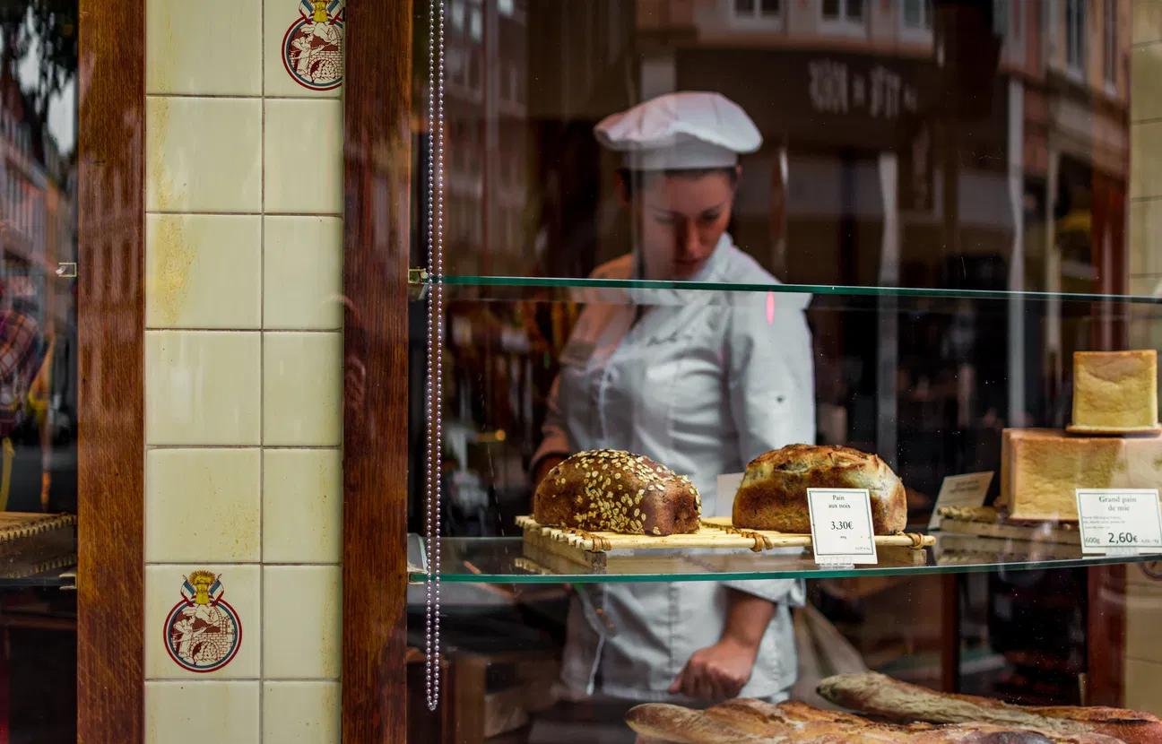 Baker in outfit examines products in the shop window.