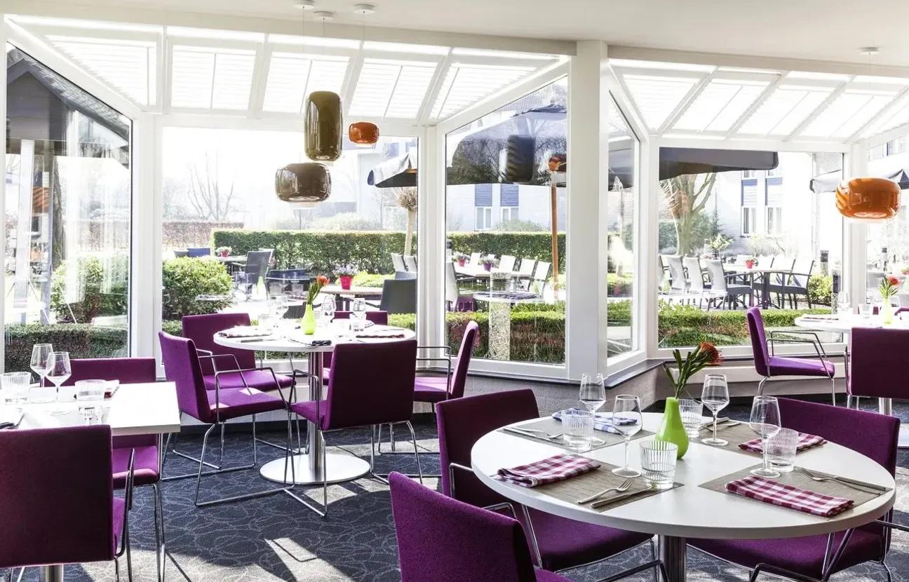 Interieur restaurant van Novotel met witte tafels en paarse stoelen