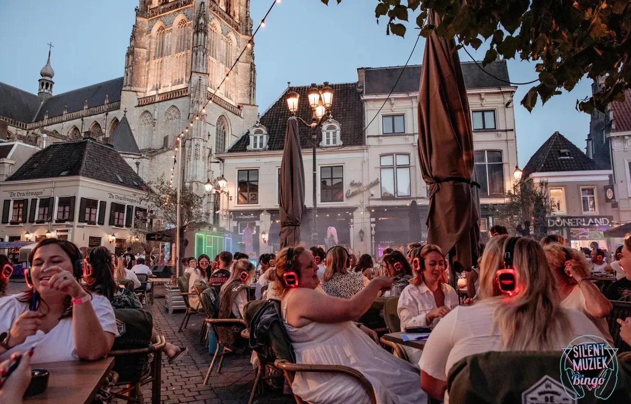 Groep mensen op de Havermarkt in Breda bij een silent disco met de Grote Kerk van Breda op de achtergrond