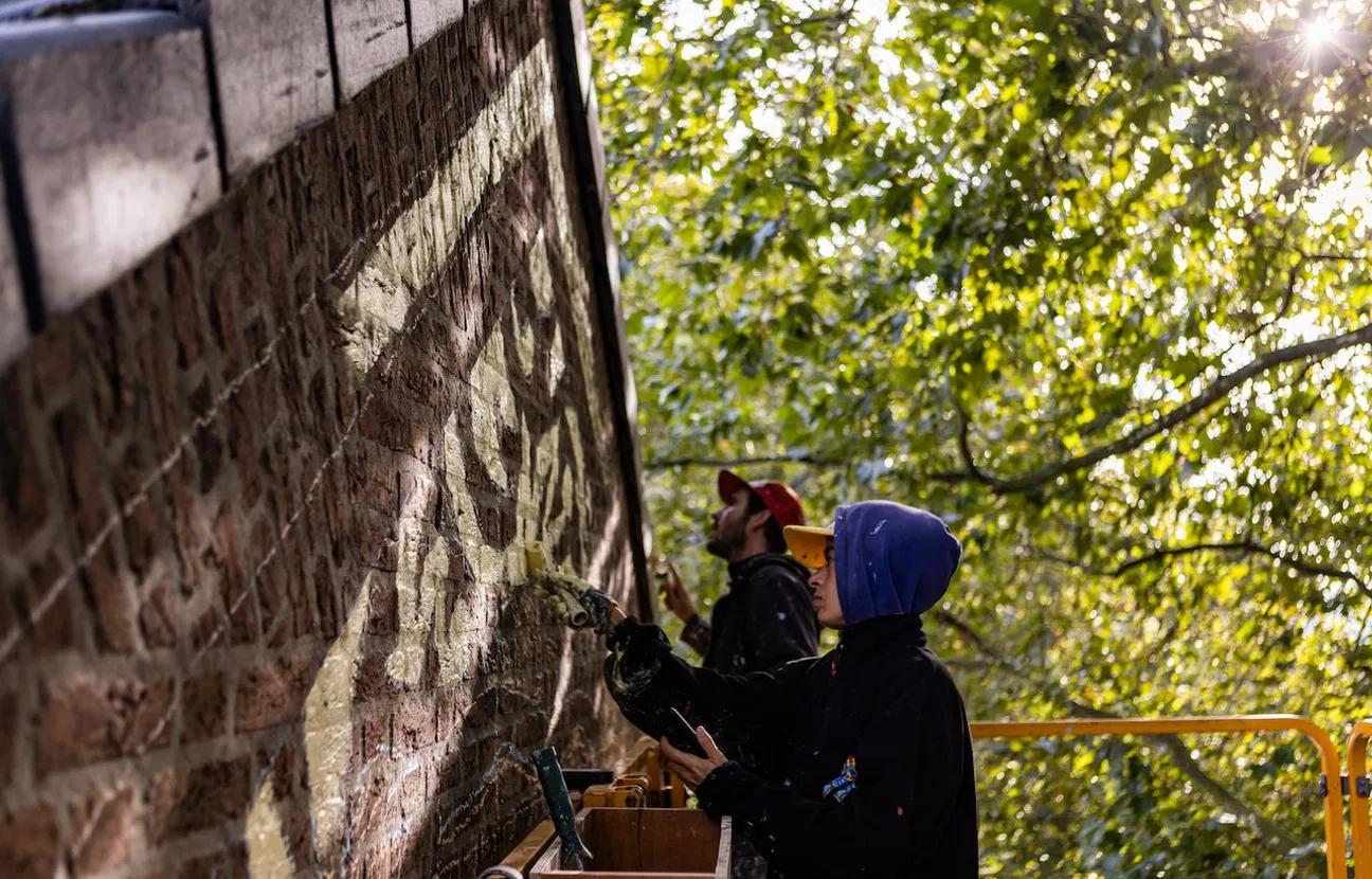 Artiest die de 100e blindwall aan het schetsen is op een bakstenen muur, foto genomen vanuit onder